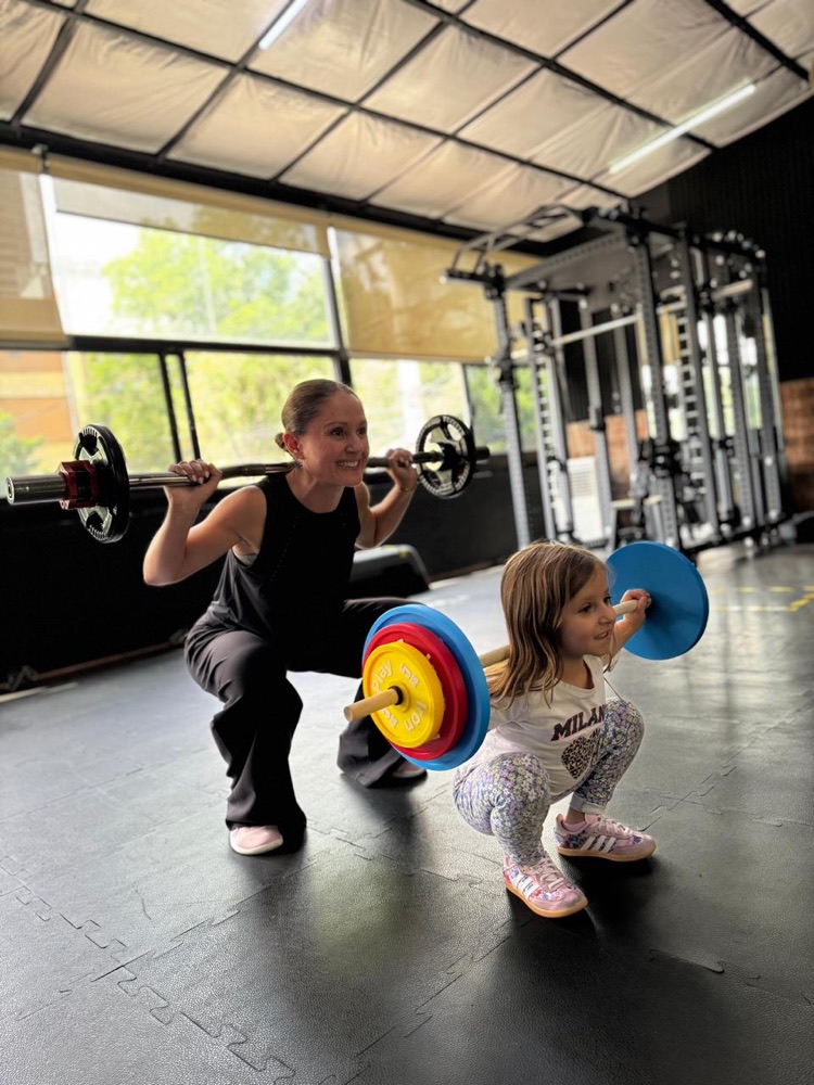 La Dra. Ligia Arechavala entrenando en el gimnasio junto a su hija, que levanta una barra infantil